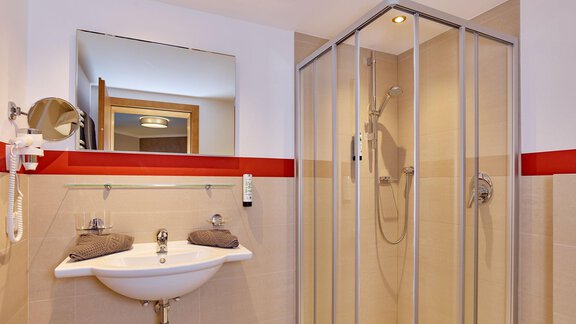 A modern bathroom with a shower and a sink. The walls are in neutral colors, with a red accent line. - Alp Resort Tiroler Adler - Sölden