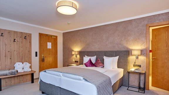 A modern hotel room with a double bed and stylish decorations. The walls are painted in warm colors and the room features wooden details as well as cozy lighting. - Alp Resort Tiroler Adler - Sölden