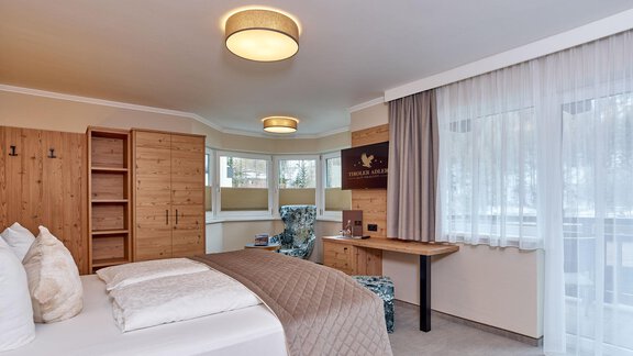 A modern bedroom with a large bed and bright curtains. Wooden shelves and a desk create a cozy atmosphere. - Alp Resort Tiroler Adler - Sölden