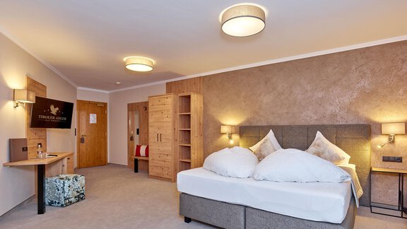 A modern hotel room with a large bed and neutral colors. On the left side, there is a desk and a television. - Alp Resort Tiroler Adler - Sölden