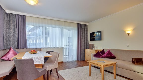 A cozy living space with a dining area and a large window. The decor is modern and bright, featuring a wooden floor and soft furnishings. - Alp Resort Tiroler Adler - Sölden