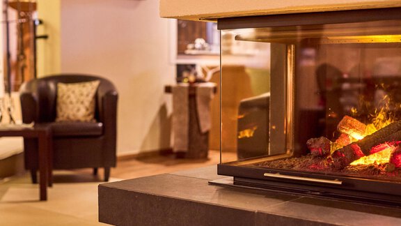 A cozy fireplace with blazing logs. In the background, there is an inviting living area with a comfortable armchair. - Alp Resort Tiroler Adler - Sölden