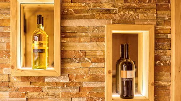 Two wine bottles are placed in illuminated niches against a stone wall. One bottle is white and the other is red. - Alp Resort Tiroler Adler - Sölden