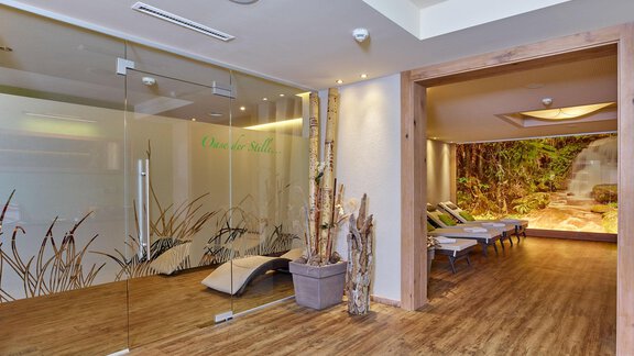 A modern wellness area with glass walls and wooden details. Relaxation loungers and a calming plant landscape create an inviting atmosphere. - Alp Resort Tiroler Adler - Sölden