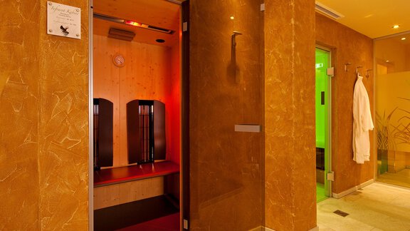An elegant wellness area with a sauna and soothing lighting. The walls are in warm earth tones, and there is a bathrobe hanging on the wall. - Alp Resort Tiroler Adler - Sölden