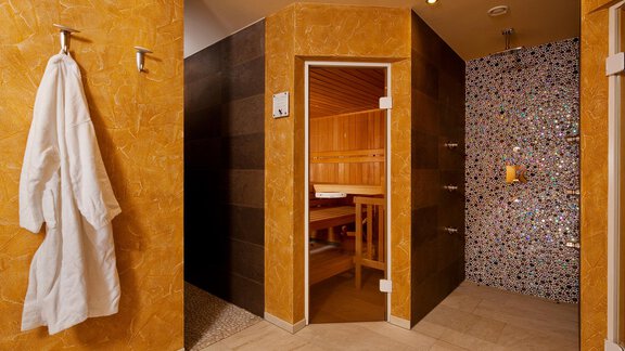 A stylish wellness area with a sauna and a modern shower. A bathrobe hangs on the wall, the walls are decorated in warm colors. - Alp Resort Tiroler Adler - Sölden