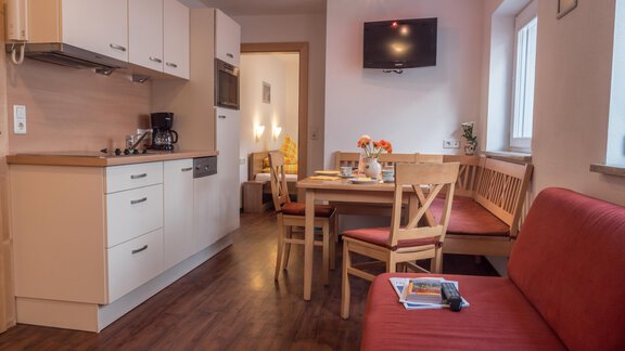 Eine gem размест уютная Wohnung mit einer modernen Küche und einem Essbereich. In der Ecke steht ein rotes Sofa und ein Fernseher ist an der Wand montiert. - Alpenapart Saphir - Sölden