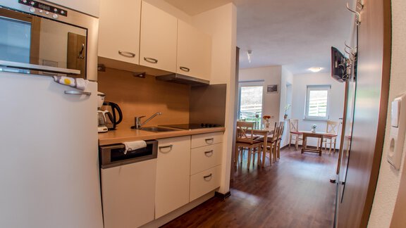 Eine moderne Küche mit weißen Schränken und Holzfußboden. Im Hintergrund ist ein Essbereich mit einem Tisch und Stühlen sichtbar. - Alpenapart Saphir - Sölden