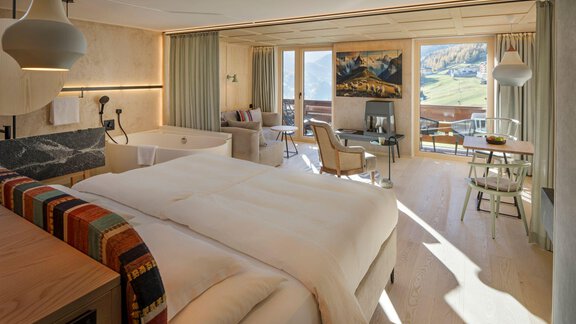 Ein modernes Hotelzimmer mit einem großen Bett und gemütlicher Sitzecke. Große Fenster bieten einen Blick auf die Berge und den Außenbereich. - Alpengasthof Grüner - Sölden