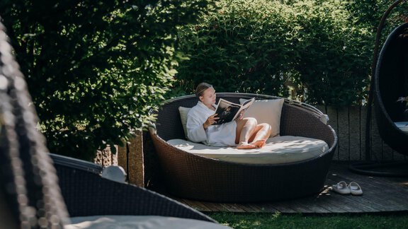 Eine Person sitzt entspannt in einem runden Liegestuhl und liest ein Buch. Die Umgebung ist grün und ruhig, ideal zum Entspannen. - Alpengasthof Grüner - Sölden