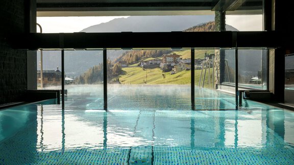 Ein elegantes Schwimmbad mit Blick auf grüne Hügel und Berge. Die Wasseroberfläche spiegelt die ruhige Atmosphäre wider. - Alpengasthof Grüner - Sölden