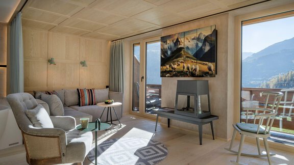 Ein modernes Wohnzimmer mit einer bequemen Couch und einem Tisch. Große Fenster bieten einen Blick auf die Berge und sorgen für viel Tageslicht. - Alpengasthof Grüner - Sölden
