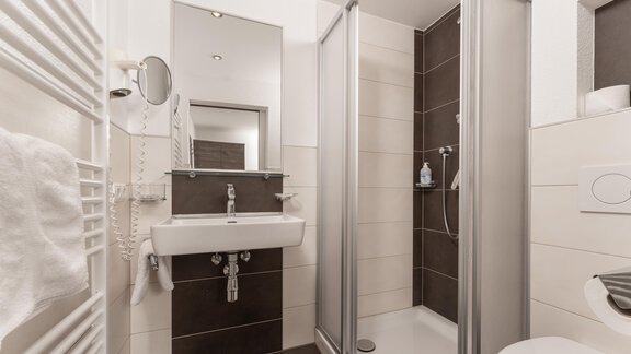 A modern bathroom with a shower and a sink. The walls are light with dark accents and there is a towel rack. - Alpenliebe - Sölden