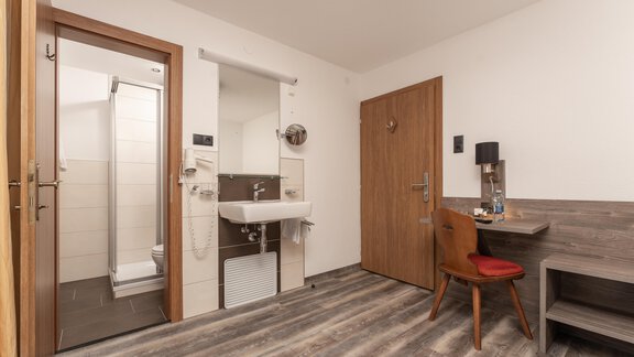 A modern room with wooden flooring, a desk, and a chair. The bathroom is separate and equipped with a shower and sink. - Alpenliebe - Sölden