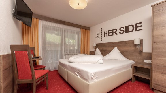 A cozy bedroom with a double bed and two red chairs. Large windows provide plenty of daylight. - Alpenliebe - Sölden
