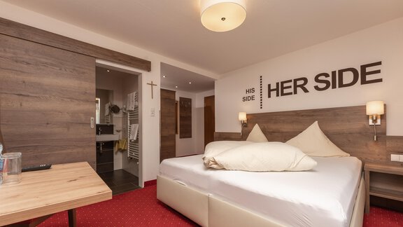 A modern bedroom with a large bed and a wooden wall. The decoration features the words "HER SIDE" and "HIS SIDE". - Alpenliebe - Sölden