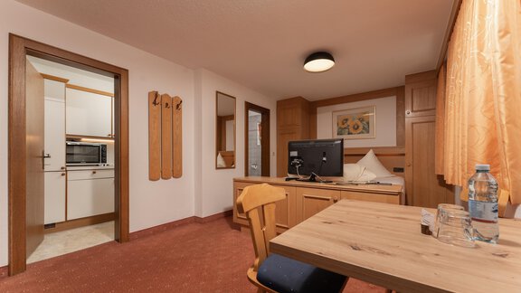 A cozy room with a wooden table and a chair. In the background, there is a small kitchen and a bed. - Alpenliebe - Sölden