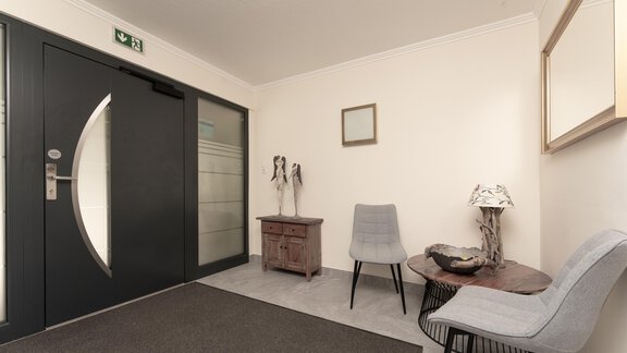 A modern foyer with gray wall color and stylish furniture. There are two chairs, a small table, and some decorative elements on the walls. - Alpenliebe - Sölden