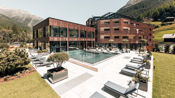 A modern hotel with a pool and outdoor loungers. Surrounded by green meadows and mountains, it offers a relaxing atmosphere. - AlpenParks The Secret Sölden - Sölden