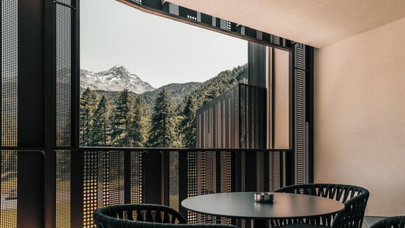 A modern balcony with a round table and chairs. In the background, you can see impressive mountains and forests. - AlpenParks The Secret Sölden - Sölden