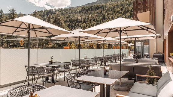 A modern terrace with seating and sun umbrellas. In the background, trees and mountains can be seen. - AlpenParks The Secret Sölden - Sölden