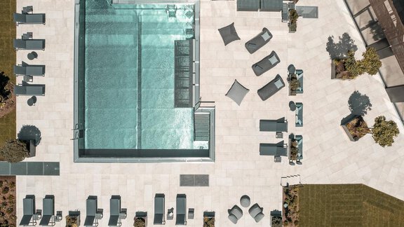 A modern-designed pool area with lounge chairs and sun umbrellas. The surroundings are decorated with green spaces and plants. - AlpenParks The Secret Sölden - Sölden