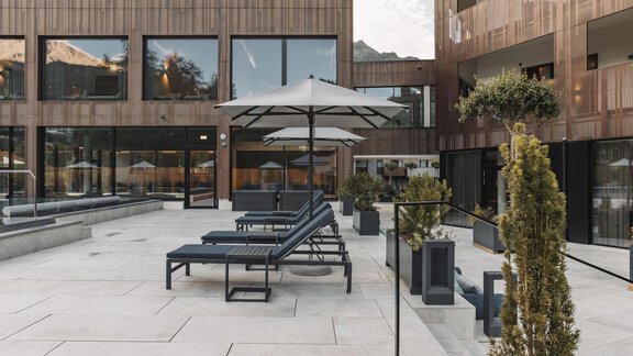 A modern terrace with sun loungers and sun umbrellas. In the background, buildings with wooden facades can be seen. - AlpenParks The Secret Sölden - Sölden