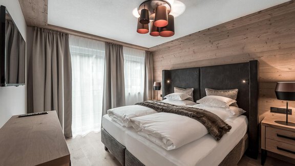 A modern bedroom with a large bed and stylish furniture.  
Large windows let in a lot of light and create a cozy atmosphere. - AlpenParks The Secret Sölden - Sölden
