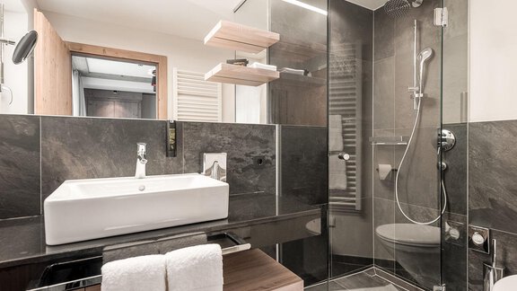A modern bathroom with elegant tiles and a glass shower. The furnishings include a stylish sink and wooden details. - AlpenParks The Secret Sölden - Sölden