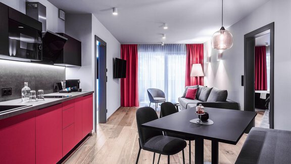 A modern apartment with red kitchen cabinet fronts and stylish furniture. The space is bright and open with large windows and a cozy dining area. - AlpenParks The Secret Sölden - Sölden