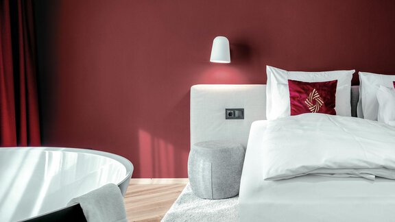 A modern bedroom with red-painted walls. The room is stylishly furnished with a cozy bed and a freestanding bathtub. - AlpenParks The Secret Sölden - Sölden