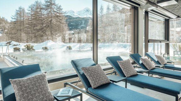 A cozy wellness area with loungers and a view of a swimming pond in a winter landscape. Outside, snow-covered trees and mountains can be seen. - AlpenParks The Secret Sölden - Sölden