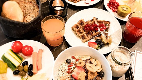 A rich breakfast buffet with various dishes, including fruit, waffles, yogurt, and bread. Fresh juices and a selection of side dishes complete the offer. - AlpenParks The Secret Sölden - Sölden