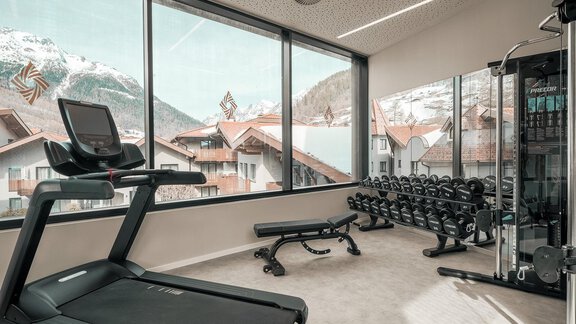 A modern gym with a view of snow-capped mountains. There is a treadmill and a weight bench with various weights. - AlpenParks The Secret Sölden - Sölden