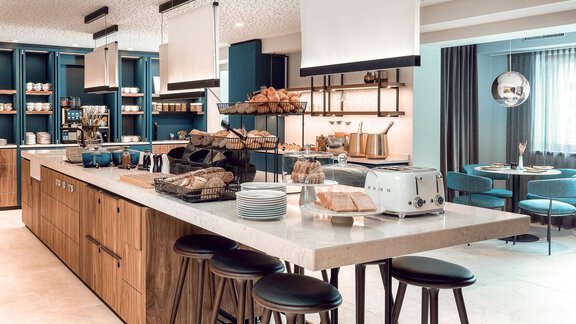 A modern kitchen with a long dining table and chairs. On the countertop, there are various foods such as bread rolls and a toaster. - AlpenParks The Secret Sölden - Sölden