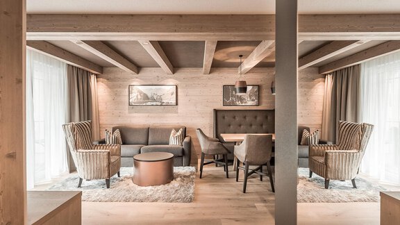 A cozy living space with modern furniture and a wooden beam ceiling. Large windows let in plenty of light and create an inviting atmosphere. - AlpenParks The Secret Sölden - Sölden