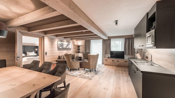 A modern living and dining room with wooden beams and elegant decor. The open kitchen blends harmoniously into the space and creates a cozy atmosphere. - AlpenParks The Secret Sölden - Sölden