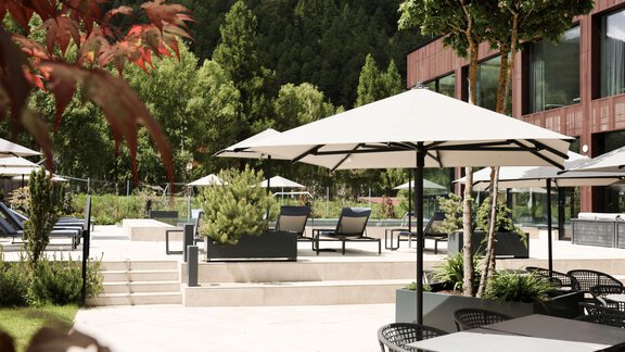 An elegant outdoor terrace with loungers and sun umbrellas. Lush green plants surround the area, creating an inviting atmosphere. - AlpenParks The Secret Sölden - Sölden