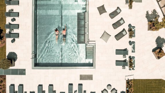 A modern swimming pool with two people swimming in the water. Elegant loungers and seating are situated around the pool on a well-maintained terrace. - AlpenParks The Secret Sölden - Sölden