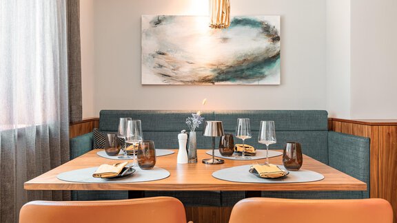 A modern dining room with a wooden table and elegant chairs. The table setting includes glasses, napkins, and a stylish piece of wall art. - AlpenParks The Secret Sölden - Sölden