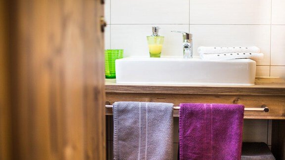 A modern bathroom with a white sink and colorful towels. On the wooden shelf are soap and a glass with a yellow liquid. - Alpensweet - Sölden