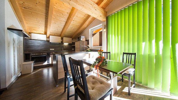 A modern dining room with a bright table and black chairs. The large green curtains let in plenty of light and create a friendly atmosphere. - Alpensweet - Sölden