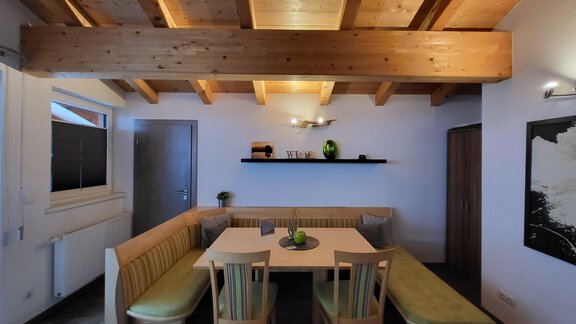 A modern dining room with a wooden beam ceiling and a cozy bench. A large table is in the center with chairs and a decorative plant. - Alpensweet - Sölden