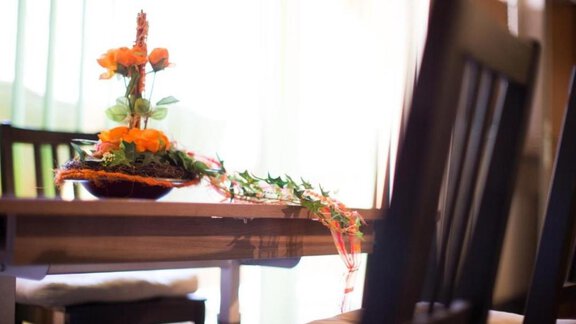 A beautifully decorated table with a floral arrangement in warm colors. The background shows bright light and windows. - Alpensweet - Sölden