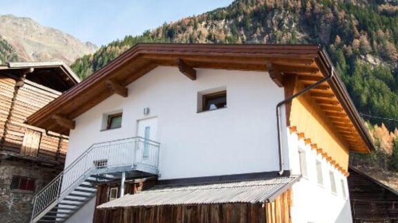 A modern house with wooden cladding and a staircase. In the background, mountains and trees can be seen. - Alpensweet - Sölden