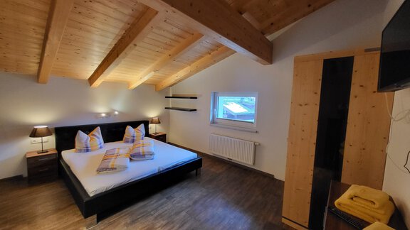 A modern bedroom with wooden ceilings and a large window. The room is cozy and stylishly furnished, with a queen-size bed and a wardrobe. - Alpensweet - Sölden