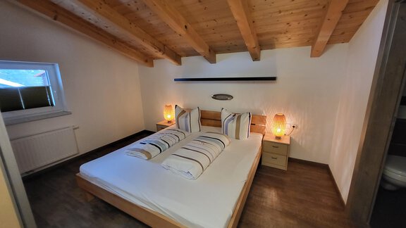 A cozy bedroom with a double bed and wooden ceiling. The room has soft light and a window that lets in daylight. - Alpensweet - Sölden