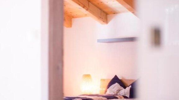 A cozy bedroom with a wooden bed and blue bedding. The room has a warm atmosphere due to soft light and visible wood grains. - Alpensweet - Sölden