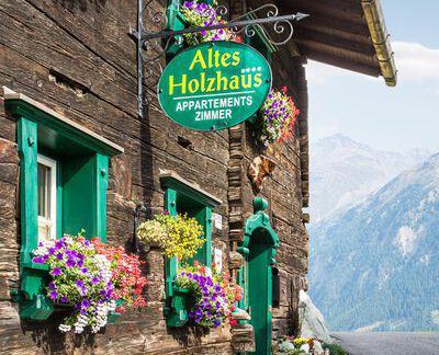 A traditional wooden house with an inviting sign and colorful flowers in front of the windows. The mountains in the background give the scene a picturesque atmosphere. - Altes Holzhaus - Sölden
