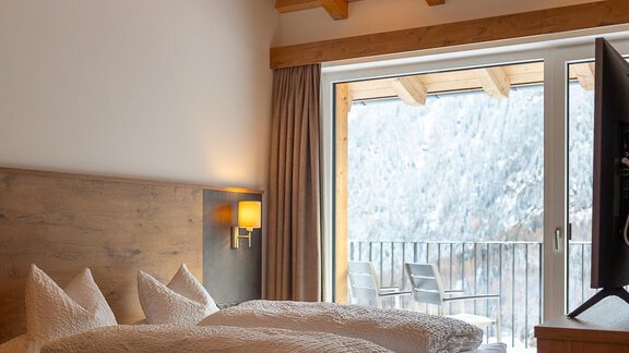 A cozy bedroom with a wooden ceiling and a large bed. The balcony offers a view of the snowy landscape. - Anraitl Appartements Sölden - Sölden